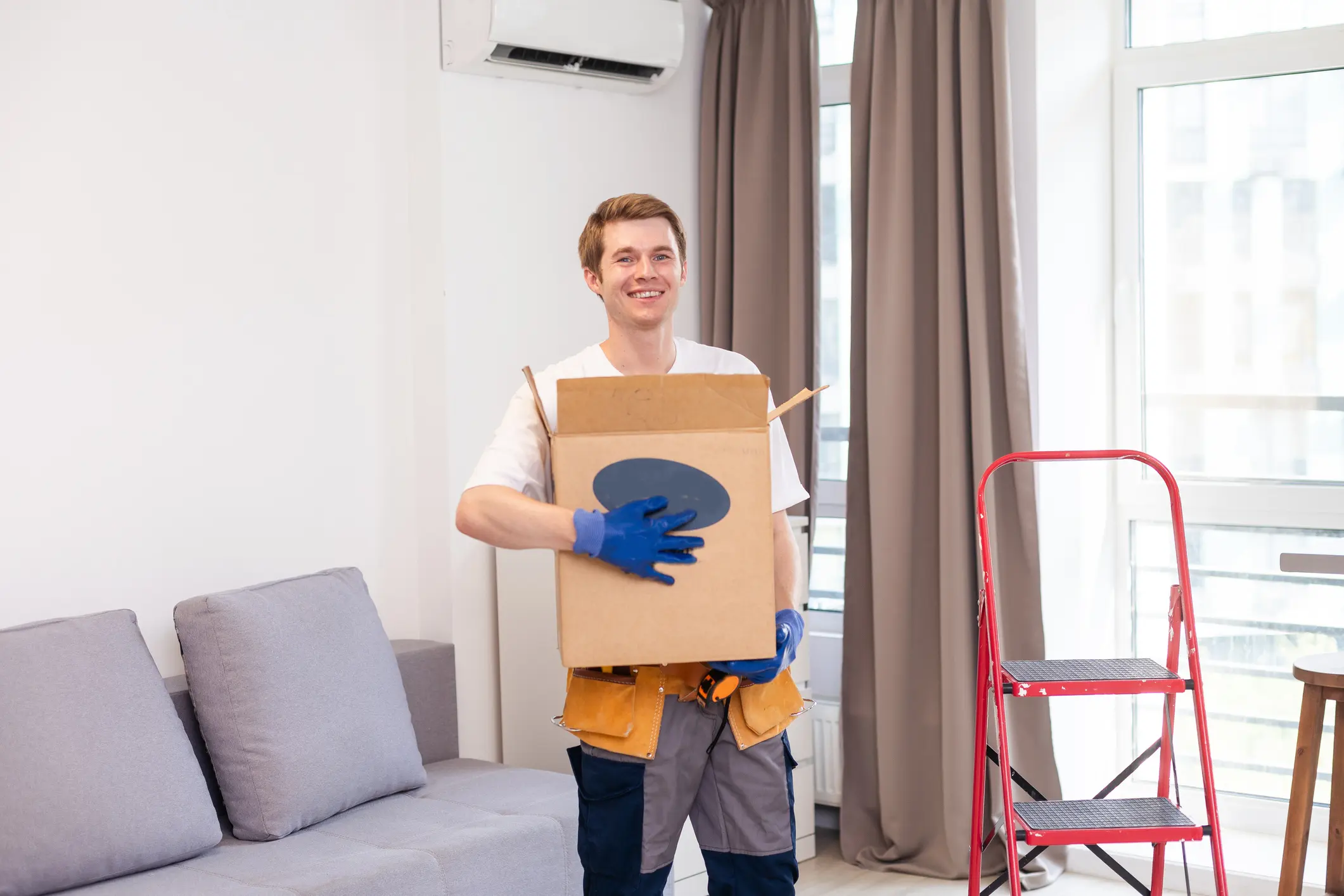 Young smiling logistic delivery man in red uniform holding the box