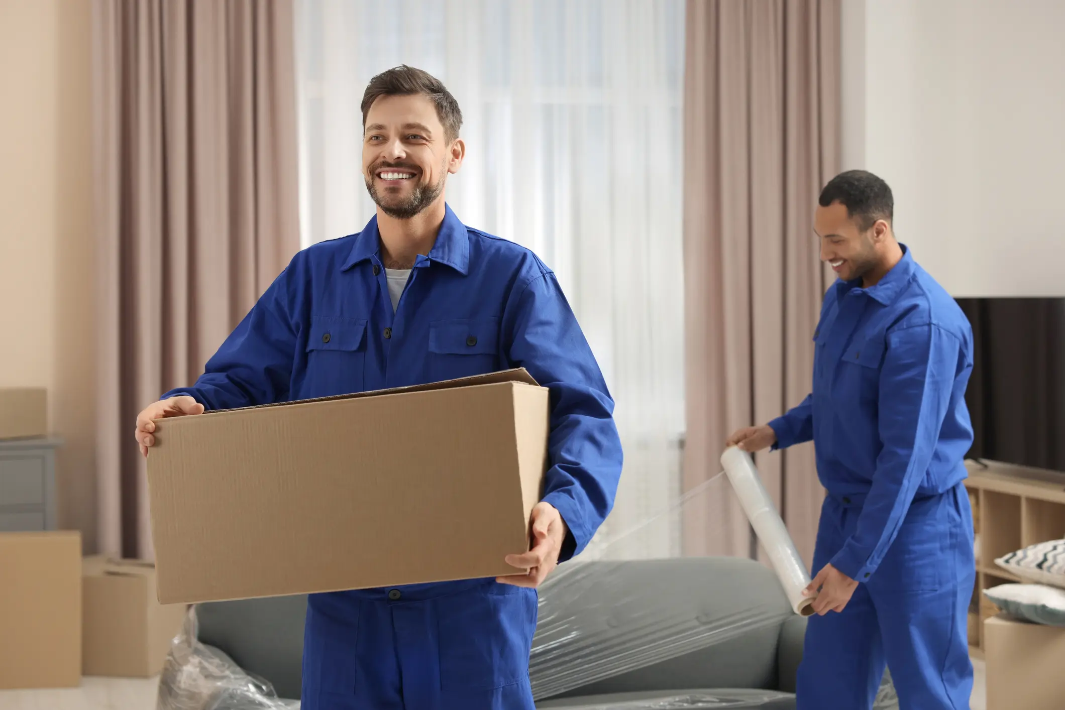 Male movers with cardboard box and sofa in new house
