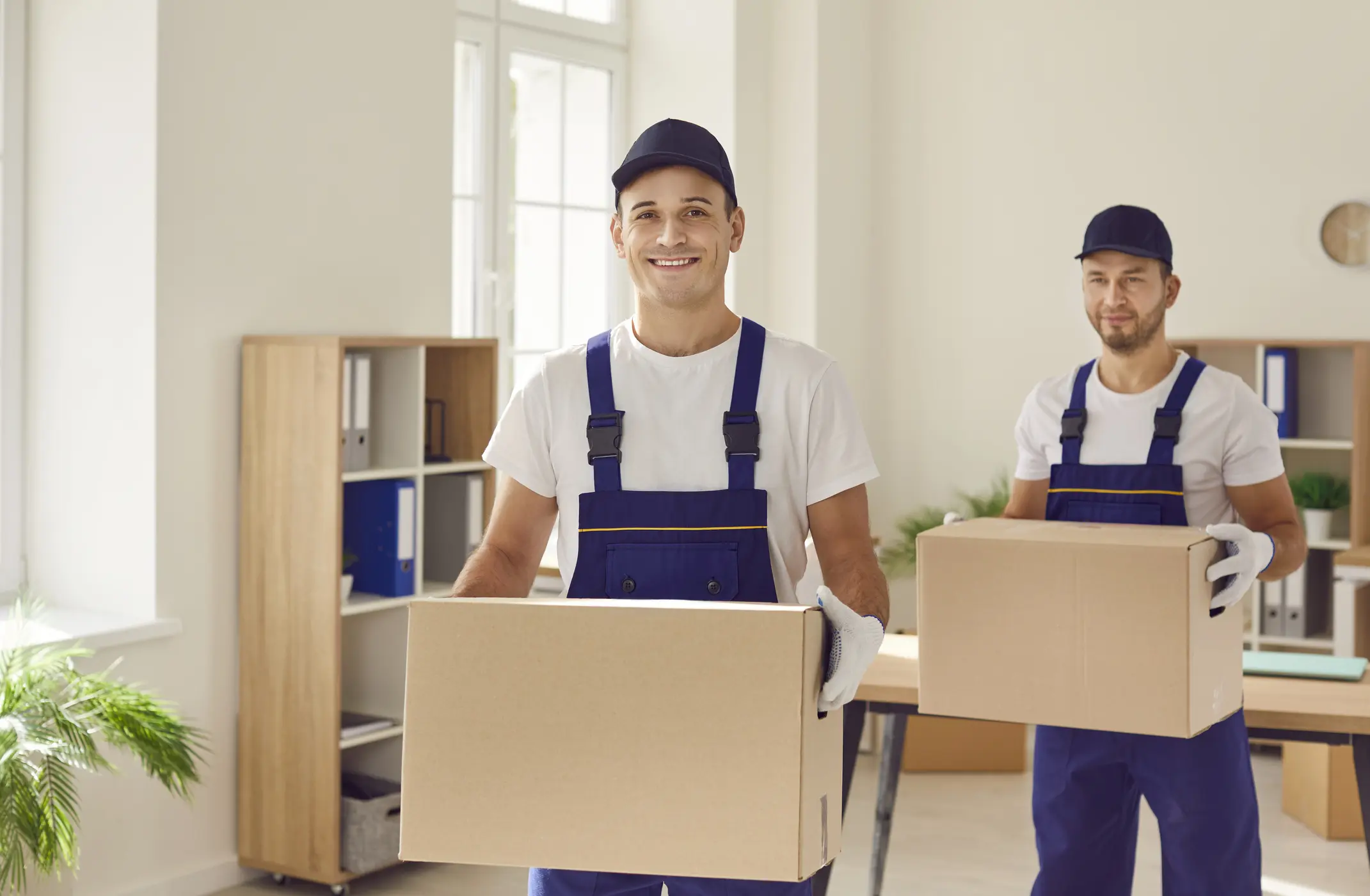 Portrait of two men, part of a relocation company, standing in an office or home. With boxes in hand, the mover staff exhibits professionalism, ready to provide top notch delivery and moving services.